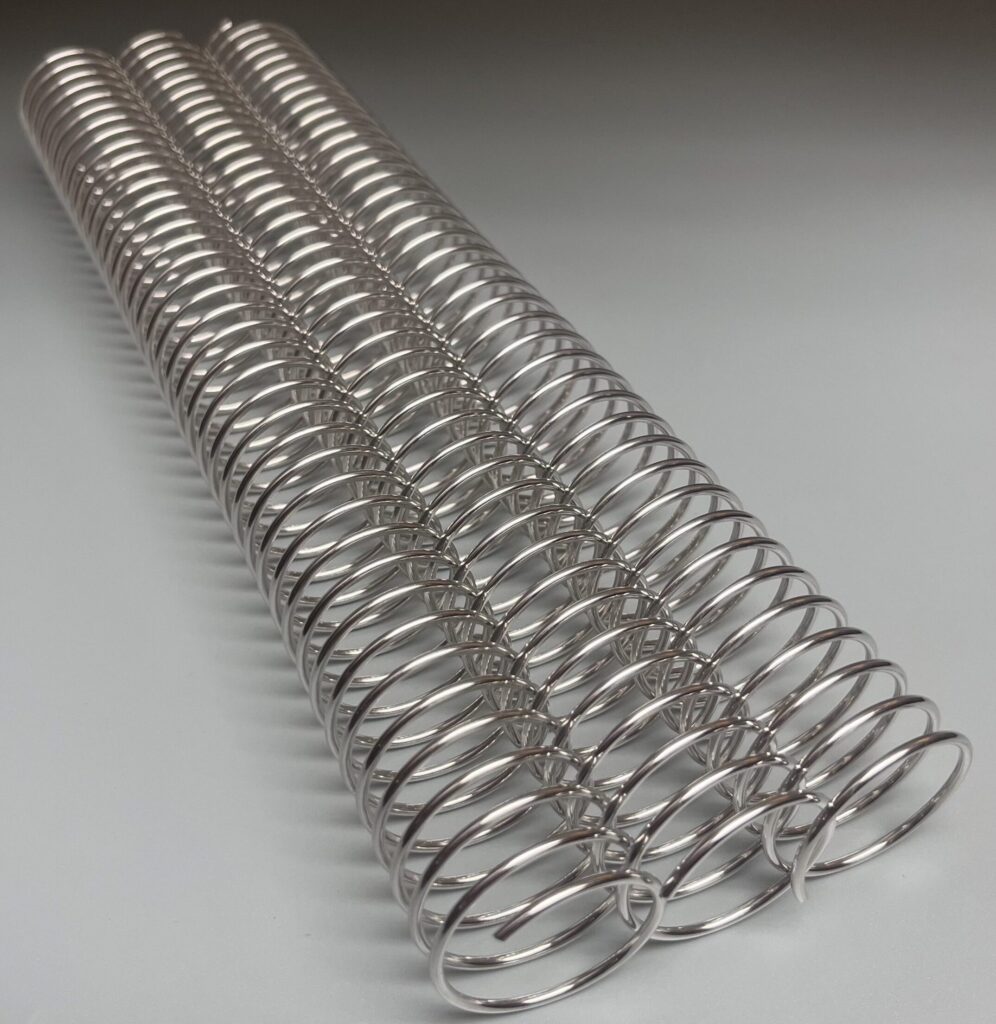 Three silver metal coil binding spines are lined up parallel on a plain gray surface.