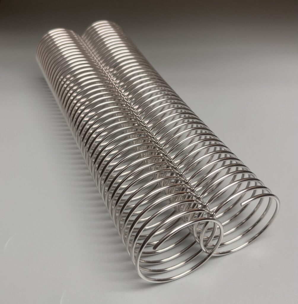 Two shiny metal coil springs are placed side by side on a smooth, light gray surface.